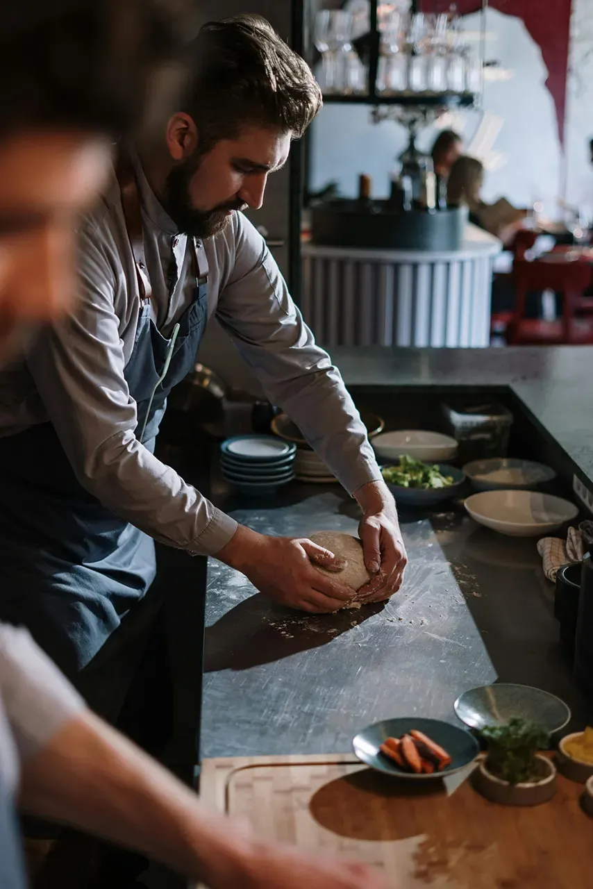 Chef kneading dough on a stainless steel countertop in a vibrant restaurant kitchen, with plates and fresh ingredients visible, emphasizing the culinary energy of Las Vegas dining.