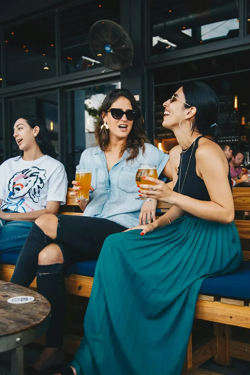 Three women enjoying drinks in a casual outdoor setting, laughing and engaging in conversation, with a focus on the vibrant social atmosphere of Las Vegas dining.